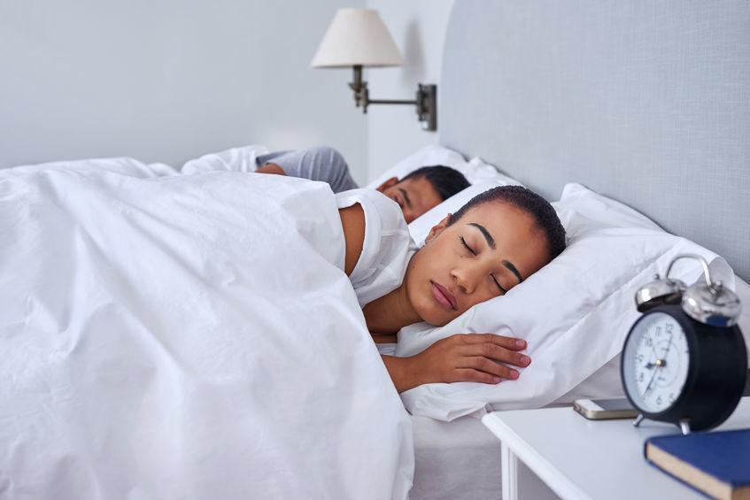 A couple sleeping in bed by alarm clock